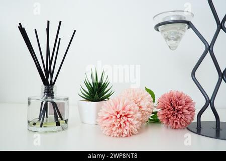 Composizione con bastoncini di incenso, olio essenziale in vaso di vetro e fiori artificiali di spugna rosa. Lampadario alto in metallo. Candela profumata a righe grigie Foto Stock