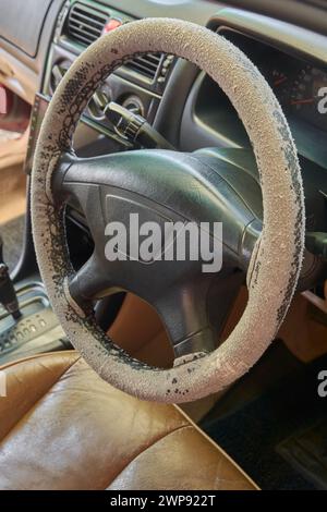 rivestimento del volante dell'auto vecchio e usurato, sbiadito a causa dell'esposizione alla luce del sole e rimosso la pelle dall'uso costante per un lungo periodo di tempo, con una messa a fuoco selettiva Foto Stock