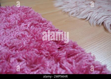 Tappeto a pelo lungo in rosa su un pavimento in laminato beige. Interni femminili per una stanza o una camera da letto di una ragazza o di una donna. Design degli interni in tonalità rosa. Pavimento Foto Stock