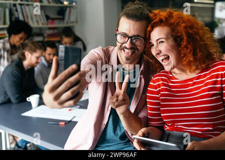 Amichevole felice collaboratore multietnico maschio e femmina divertirsi con lo smartphone, lavorando insieme Foto Stock