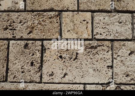 Parete testurizzata rivestita con piastrelle in pietra beige. Primo piano di un muro fatto di antica roccia a conchiglia. Buchi, irregolarità del materiale da costruzione naturale Foto Stock