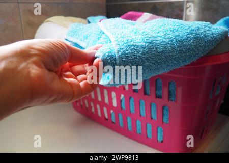 La mano di una donna sente un asciugamano di cotone colorato da un cesto con bucato sporco. Lavanderia selezione e lavaggio. Lavanderia o bagno. Servizio di pulizia Foto Stock