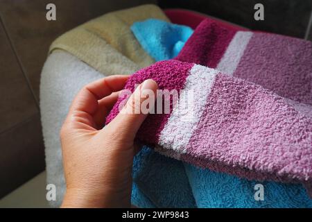 La mano di una donna sente un asciugamano di cotone colorato da un cesto con bucato sporco. Lavanderia selezione e lavaggio. Lavanderia o bagno. Servizio di pulizia Foto Stock