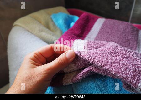 La mano di una donna sente un asciugamano di cotone colorato da un cesto con bucato sporco. Lavanderia selezione e lavaggio. Lavanderia o bagno. Servizio di pulizia Foto Stock