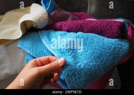 La mano di una donna sente un asciugamano di cotone colorato da un cesto con bucato sporco. Lavanderia selezione e lavaggio. Lavanderia o bagno. Servizio di pulizia Foto Stock