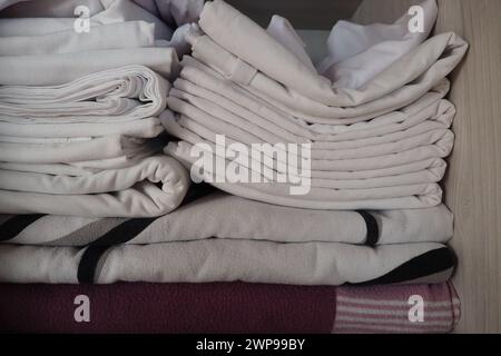 Le lenzuola bianche sono impilate nell'armadio. Contenuto interno di un armadio di lino. Organizzazione domestica. Condizioni igieniche per il sonno. Tessuti e. Foto Stock