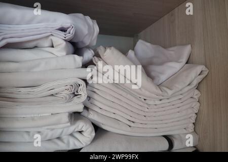 Le lenzuola bianche sono impilate nell'armadio. Contenuto interno di un armadio di lino. Organizzazione domestica. Condizioni igieniche per il sonno. Tessuti e. Foto Stock