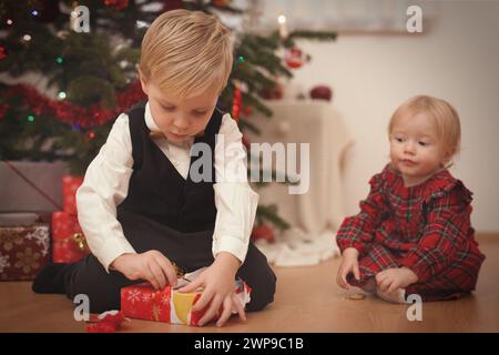 Bambini al momento del giorno di natale che disimballano i regali vicino all'albero Foto Stock