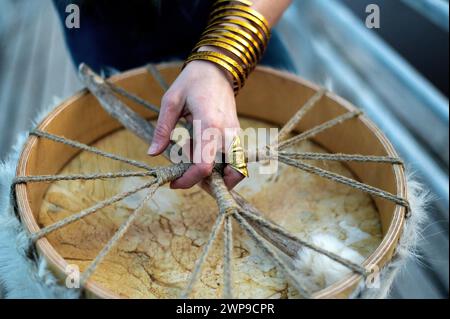 Primo piano di una mano di sciamano che tiene in mano il tamburo sciamanico, il bracciale dorato e gli anelli Foto Stock