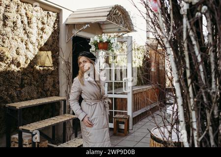 Una figura femminile vestita con un lungo cappotto si erge con sicurezza di fronte a un edificio torreggiante. Foto Stock