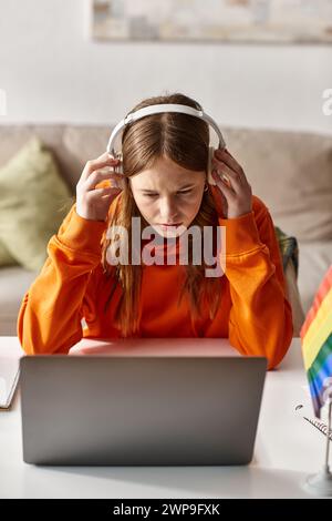 adolescente che indossa le cuffie e l'e-learning accanto al laptop e alla bandiera pride sulla scrivania Foto Stock