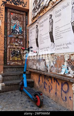 Moderno scooter elettrico a noleggio, parcheggiato vicino a una porta dipinta con graffiti all'angolo di una strada nel quartiere Trastevere. Roma, Italia, Europa Foto Stock