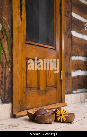 Un paio di vecchi zoccoli con cinturino marrone in pelle davanti alla porta d'ingresso posteriore sulla vecchia cabina in legno ricostruita. Foto Stock