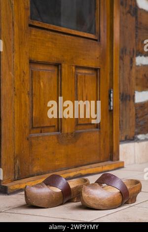 Un paio di vecchi zoccoli con cinturino marrone in pelle davanti alla porta d'ingresso posteriore sulla vecchia cabina in legno ricostruita. Foto Stock