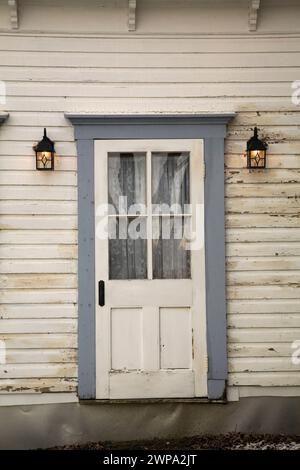Porta d'ingresso anteriore con finiture grigie e lampade da parete illuminate su una vecchia lavagna bianca rivestita in casa. Foto Stock