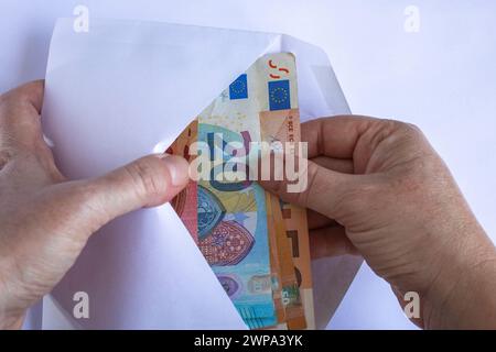 Le mani della donna caucasica prendono banconote da 10, 20 e 50 euro da una busta bianca Foto Stock