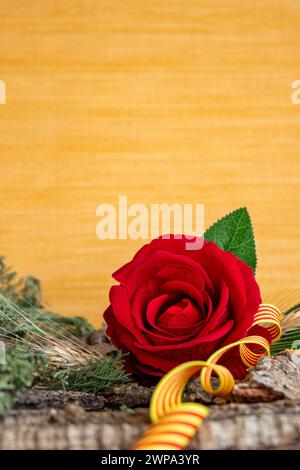 Tessera verticale di una rosa rossa con un nastro della bandiera della Catalogna sulla corteccia di un albero. Sfondo texture giallo Foto Stock
