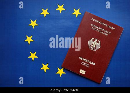Passaporto tedesco rosso dell'Unione europea su sfondo bandiera blu primo piano. Concetto di turismo e cittadinanza Foto Stock