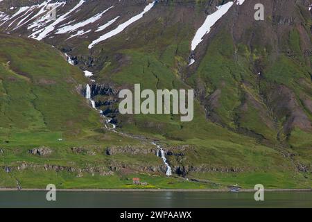 Cascata e fattoria desolata lungo il fiordo Seyðisfjörður / Seydisfjoerdur in estate, regione orientale / Austurland, Islanda Foto Stock