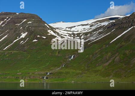 Cascata e fattoria desolata lungo il fiordo Seyðisfjörður / Seydisfjoerdur in estate, regione orientale / Austurland, Islanda Foto Stock