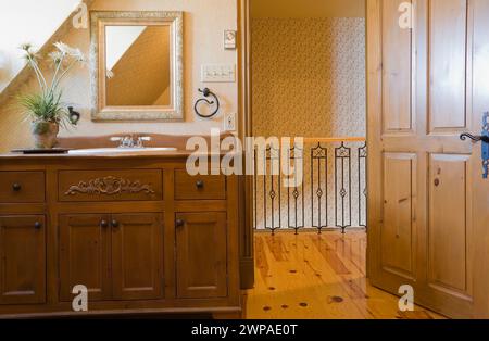 Antico lavandino in legno colorato marrone con lavandino bianco e rubinetti in porcellana nel bagno al piano superiore all'interno di una vecchia casa. Foto Stock