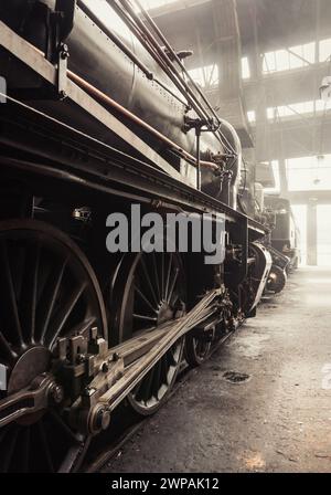 Era del vapore - vecchia locomotiva a vapore nel capannone dei treni. Locomotiva a vapore in deposito. Immagine con toni caldi (quasi seppia). Spazio interno del deposito pieno di fumo. Foto Stock