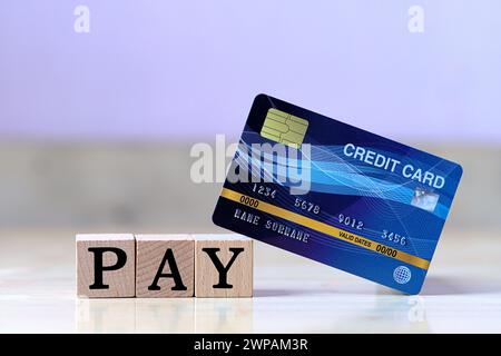Carta di credito blu e lettera a forma di cubo di legno su un tavolo di legno con spese tramite carta di credito invece che contanti Foto Stock