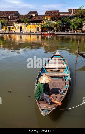 Hoi An, Vietnam; Una donna che si rilassa nella sua barca di legno. Sullo sfondo: Alcuni dei numerosi edifici conservati e trasformati in boutique o negozio Foto Stock