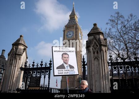 Come cancelliere del partito conservatore Jeremy Hunt consegna il suo bilancio pre-elettorale, un manifestante anti-governo si erge con un cartello parodia fuori dal parlamento, il 6 marzo 2024, a Londra, in Inghilterra. Foto Stock