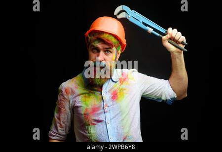 Operaio edile o costruttore in elmetto con chiave per tubi regolabile. Uomo con barba in casco protettivo con chiave regolabile. Tecnico, riparatore Foto Stock