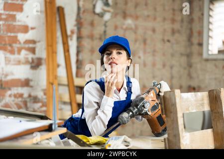 Costruttore femminile che tiene con sicurezza il martello pneumatico in casa in fase di costruzione Foto Stock
