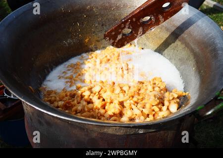 Mescolare il grasso in una grande vasca sulla legna da ardere. Crocchette di maiale, fritte nel grasso, cotte al forno, tostate per produrre cracklings o graffiature di maiale. Marrone tostato Foto Stock