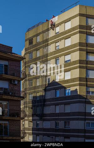 Operai appesi a corde che ridipingono il muro della facciata di un tipico edificio in stile modernista nella città di Villarreal, Comunità Valenciana, Spagna. Foto Stock