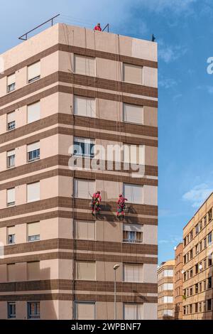 Operai appesi a corde che ridipingono il muro della facciata di un tipico edificio in stile modernista nella città di Villarreal, Comunità Valenciana, Spagna. Foto Stock