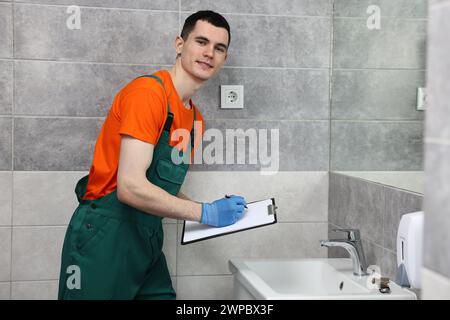 Giovane idraulico che scrive i risultati dell'esame del lavandino in bagno Foto Stock