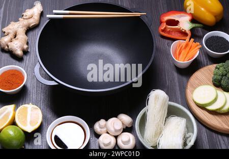 Wok, bacchette e ingredienti vuoti su un tavolo di legno grigio scuro Foto Stock