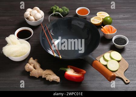 Wok e bacchette vuote circondati da ingredienti su un tavolo di legno grigio scuro Foto Stock