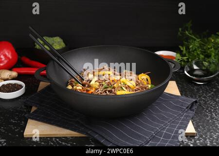 Friggere in padella. Gustosi spaghetti con verdure, carne e bacchette nel wok su un tavolo con superficie scura Foto Stock