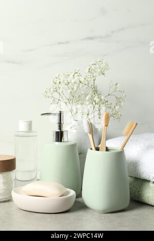 Diversi accessori per il bagno, prodotti per la cura personale e fiori di gypsophila in vaso su tavolo grigio vicino alle pareti in marmo bianco Foto Stock