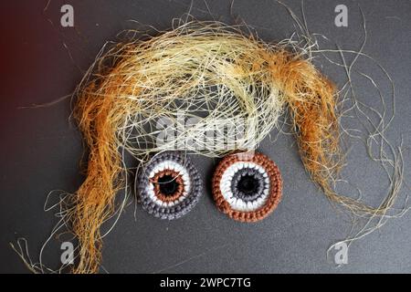 Scherzando con il volto divertente dell'arte culinaria, i capelli di seta di mais con due occhi all'uncinetto rendono divertente lo sfondo grigio Foto Stock