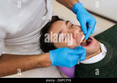 Ritratto di un giovane uomo sorridente che ha i denti controllati dal dentista durante l'appuntamento presso la clinica odontoiatrica. Primo piano dell'esame del dentista maschile irriconoscibile Foto Stock