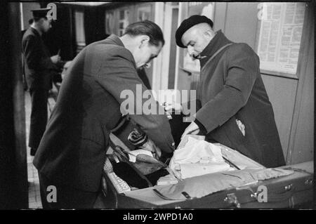 Fotografia che mostra il funzionario doganale e il viaggiatore durante l'ispezione del passaporto e dei bagagli presso la stazione estera dell'aeroporto di Varsavia, scattata da Wiesław Prażuch nel 1959 per il "Please Open!" serie. Foto Stock