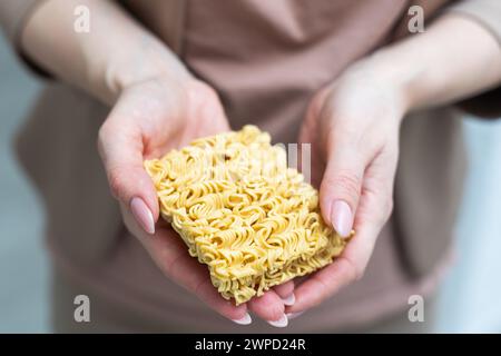 Mano che regge spaghetti gialli essiccati su sfondo bianco. Foto Stock