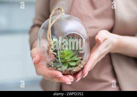 Donna che tiene un vaso di vetro con composizione vegetale all'interno, primo piano Foto Stock