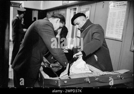 Fotografia che mostra l'agente doganale che interagisce con un viaggiatore durante il controllo dei passaporti e dei bagagli presso la stazione estera dell'aeroporto di Varsavia, parte di "Please Open!" di Wiesław Prażuch del 1959 serie di fotogiornalismo. Foto Stock