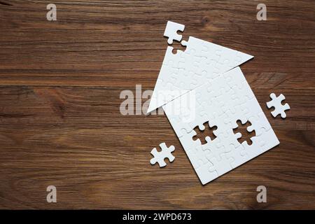 Primo piano di una casa a forma piatta realizzata con elementi puzzle con alcuni pezzi finali da posizionare, isolati su uno sfondo di legno scuro con c Foto Stock