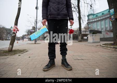 Il giovane ragazzo ucraino detiene una bandiera dell'Ucraina e fiori funebri alla cerimonia commemorativa del giorno degli Eroi dei cento celesti. Kiev - 20 febbraio 2024 Foto Stock