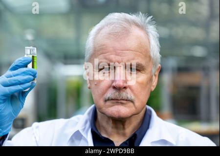 Uno scienziato anziano che tiene in mano una fiasca guarda seriamente nella telecamera. Foto Stock