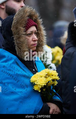 Donna Ucraina patriottica che indossa una bandiera nazionale e tiene in mano un mazzo di fiori funebri nel giorno degli Eroi dei cento celesti. Kiev - 20 febbraio 2024 Foto Stock