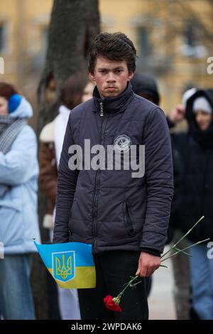 Giovane ragazzo ucraino che posa con una bandiera dell'Ucraina e un fiore funebre nel giorno degli Eroi dei cento celesti. Kiev - 20 febbraio 2024 Foto Stock